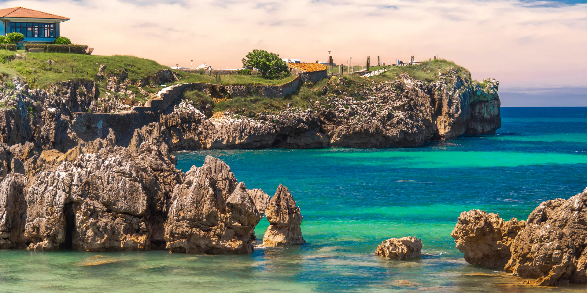 A rocky headland above turquoise water, with a white house on the cliff.