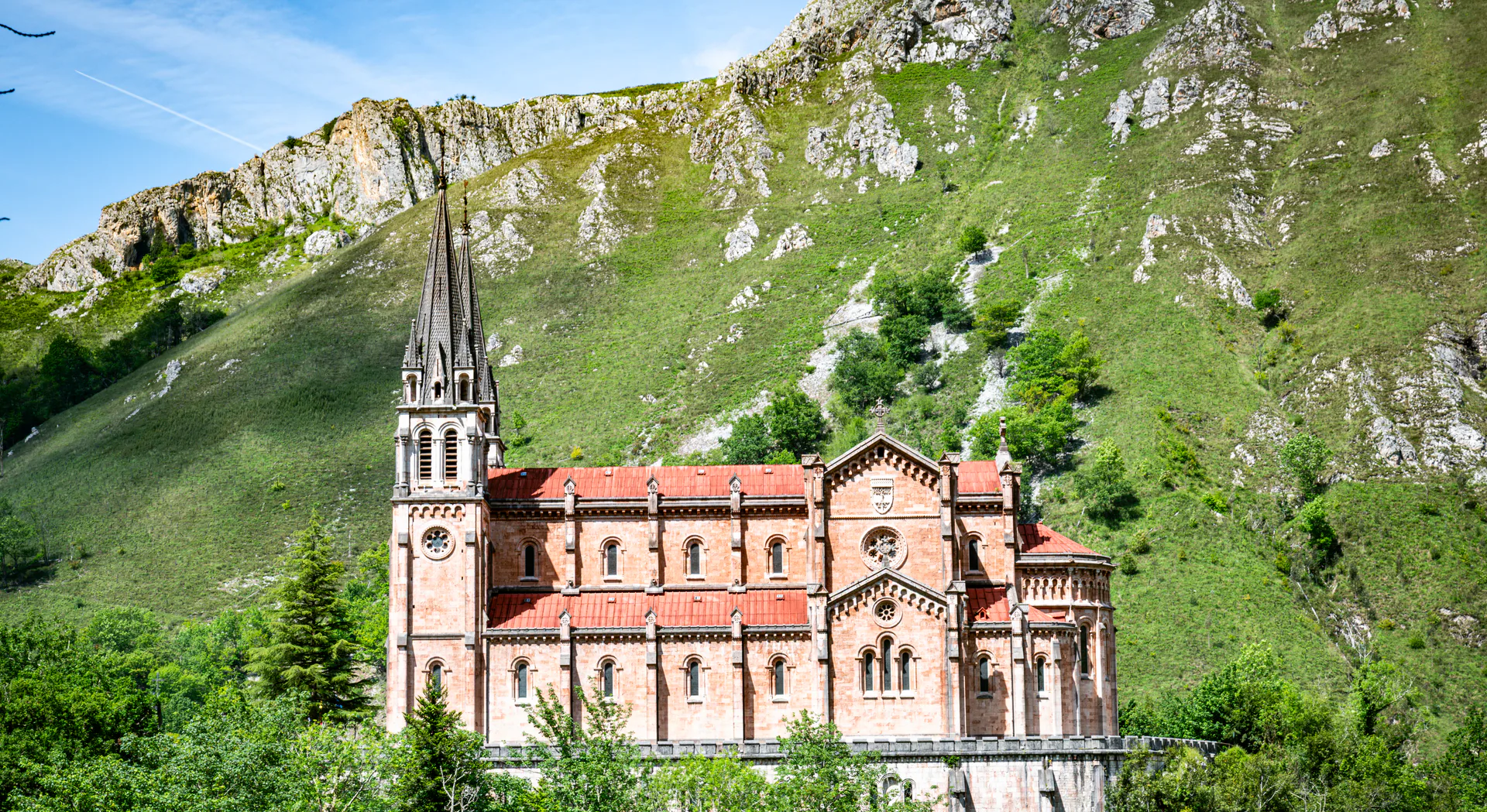 A stone basilica with a tall spire against a green mountain